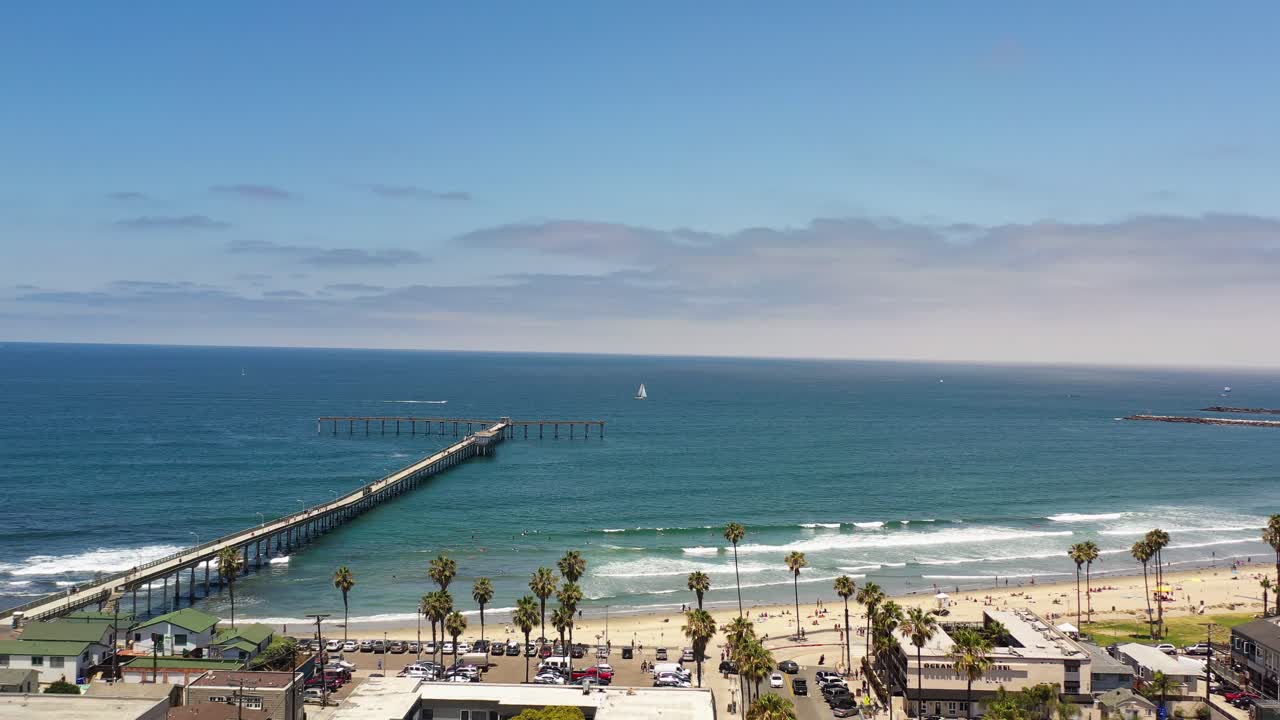 Drone subindo acima da Newport Avenue em Ocean Beach, San Diego, em direção ao píer com surfistas visíveis no oceano