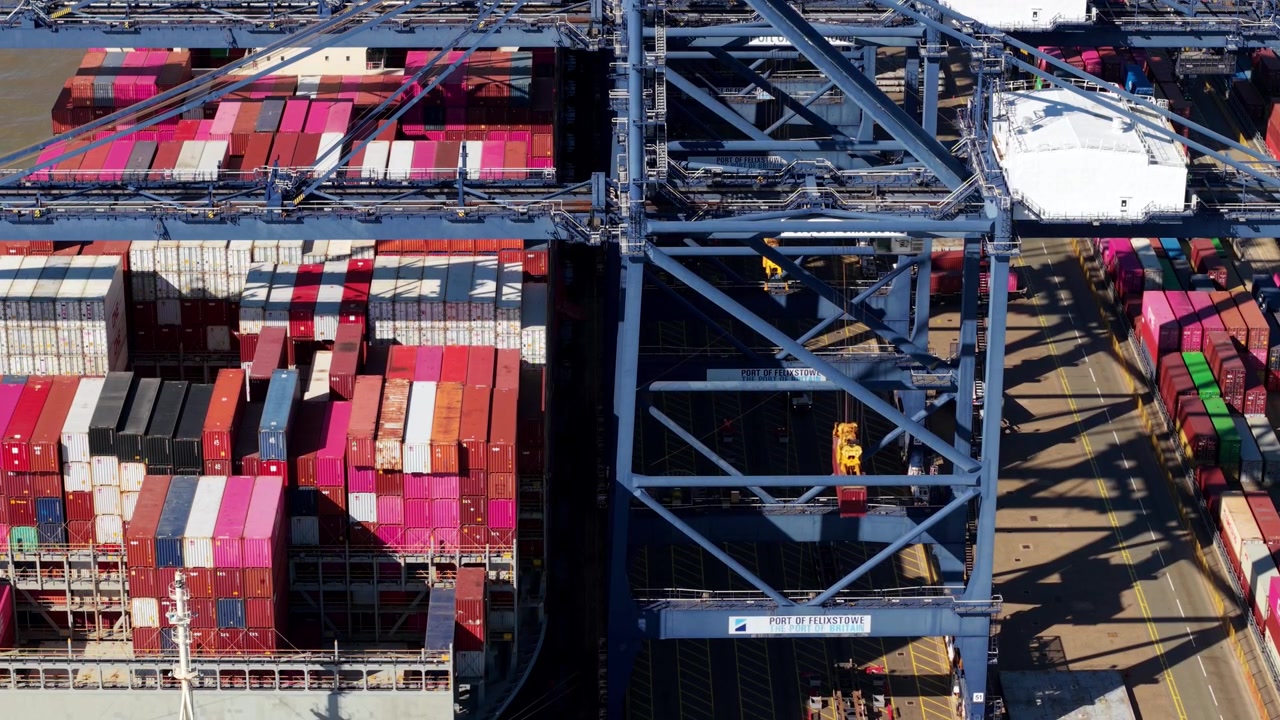 Slow aerial orbit around giant ship to shore cranes loading container ships at Felixstowe container terminal