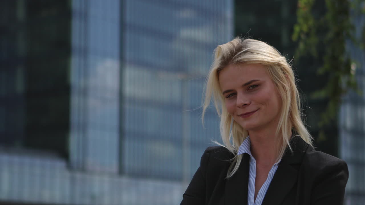 A young corporate employee, a manager, stands in the street confident and looks at the camera