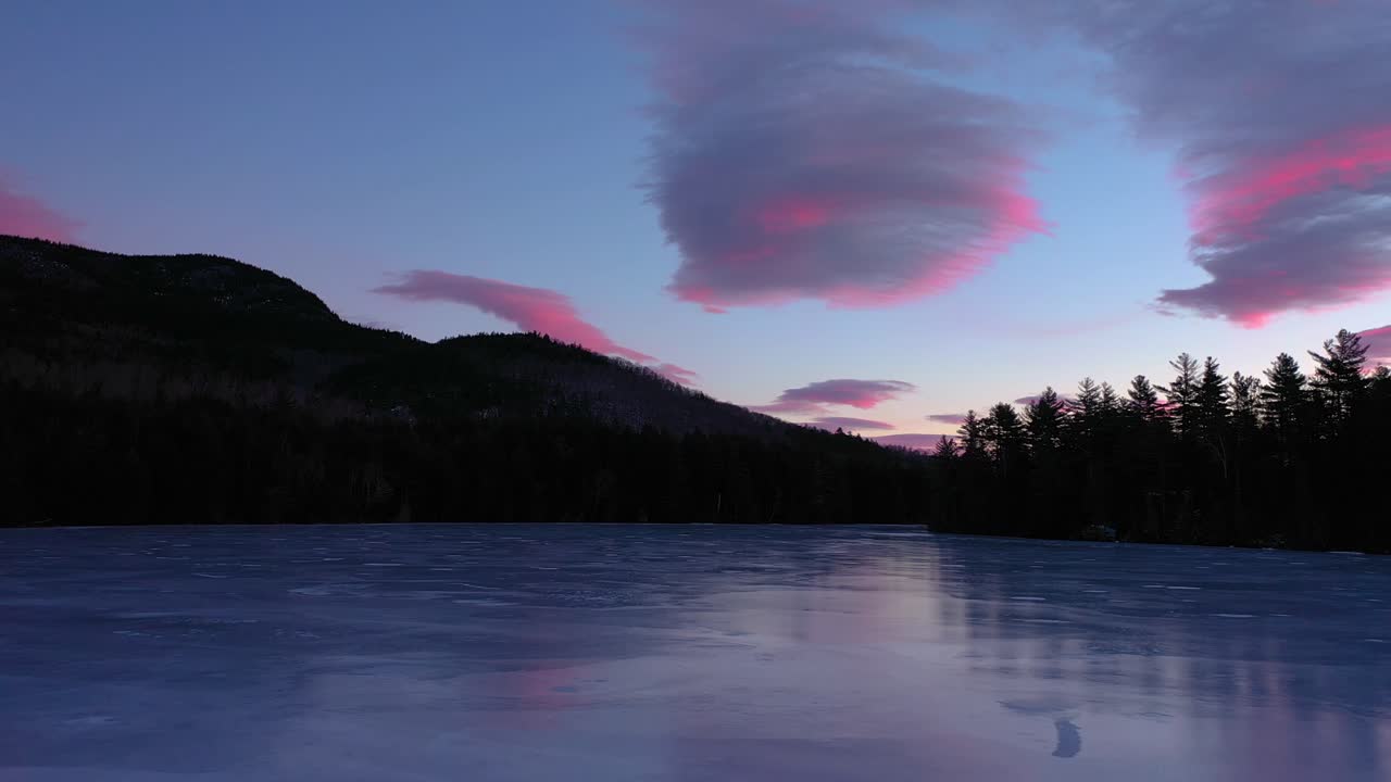 Aerial footage flying low across the surface of a frozen pond towards pink and blue cotton candy clouds