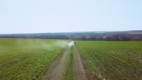 vista cinematográfica aérea de un coche de la ciudad conduciendo a través del campo verde y la carretera de tierra