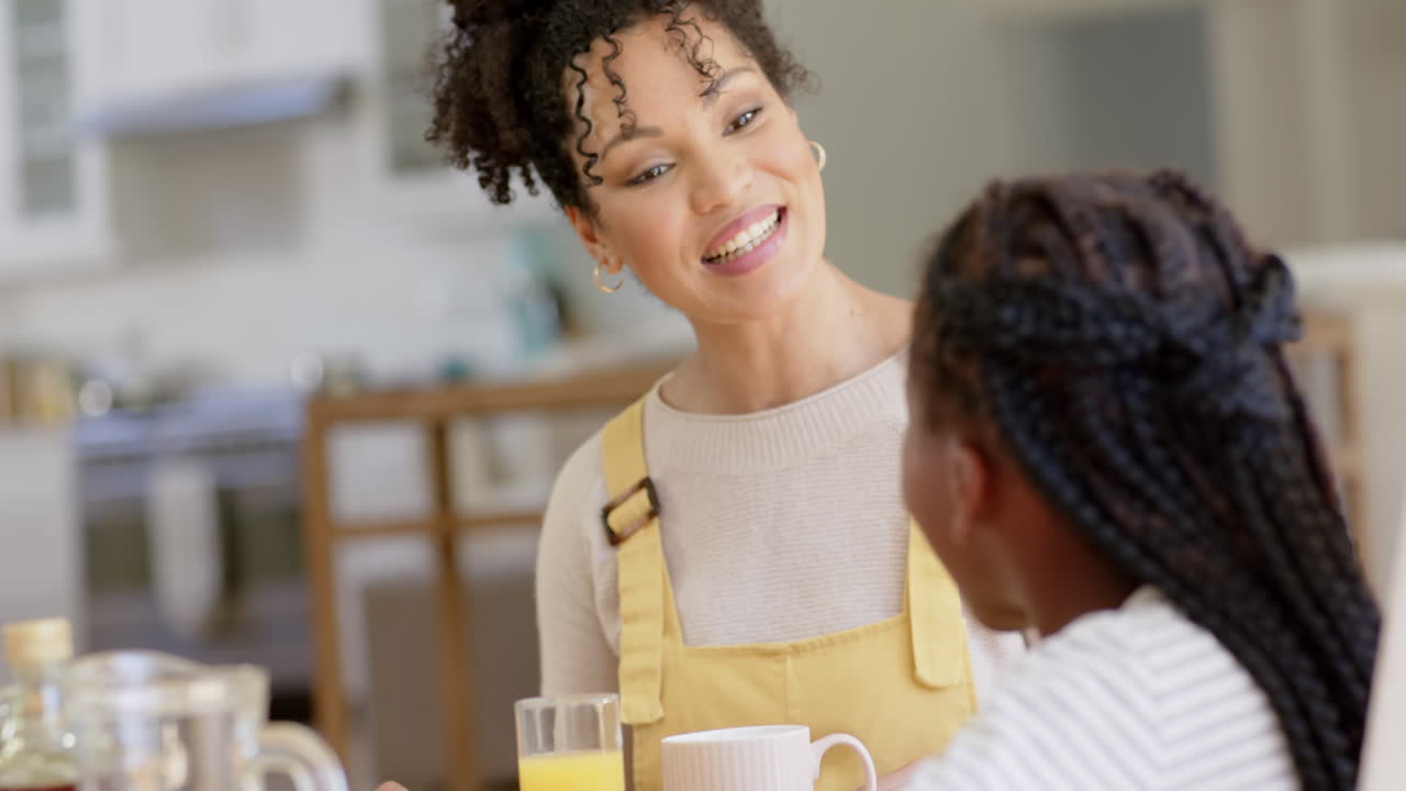 Glückliche afroamerikanische Mutter und Tochter unterhalten sich und frühstücken zu Hause, Zeitlupe.