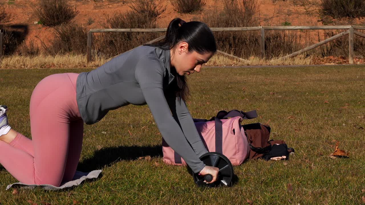 Close-up of fit woman exercising with abdominal wheel outdoors on grass, 4K