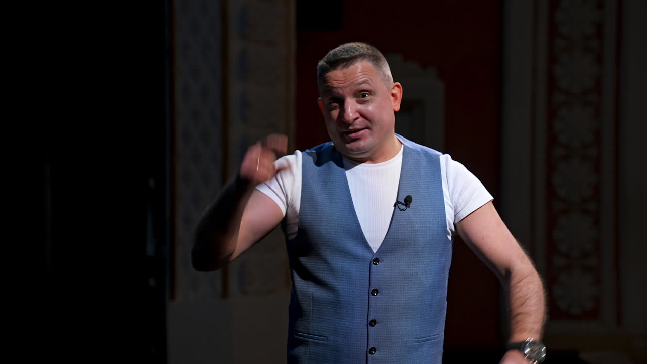 Public speaker gives performance. Middle age male entertainer, presenter or actor on stage. Man in theater wears handfree microphone.