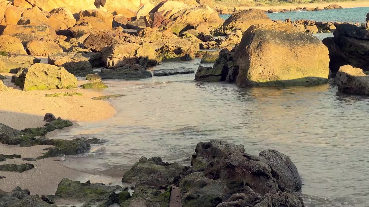 Luce dell'ora d'oro che illumina l'acqua dell'oceano che scorre tra le rocce su una spiaggia sabbiosa, Barbate, Spagna.
