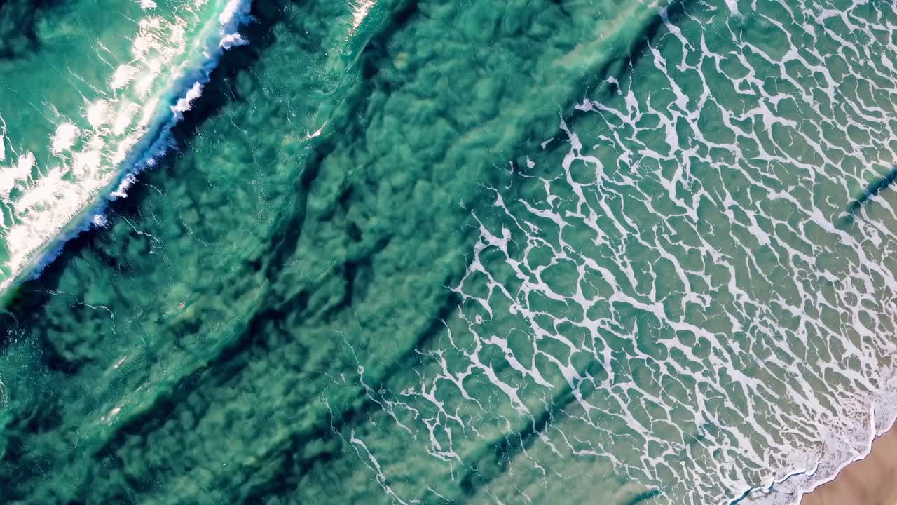 Aerial view of ocean waves gently crashing on the shore, captured in a serene, high-angle video