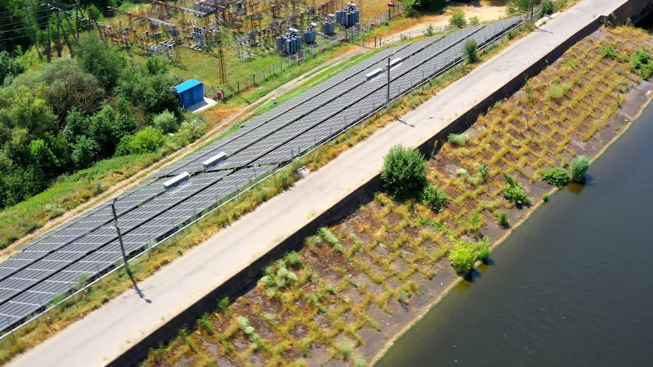 Solar farm near the river. Blue solar panels on the bank of the river in a sunny daytime. Electric power station generate clean energy from the sun. Aerial view.