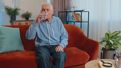 Un-Anciano-Sediento-Sentado-En-Su-Casa-Sosteniendo-Un-Vaso-De-Agua-Natural-Haciendo-Sorbos-Bebiendo-Agua-Sin-Gas