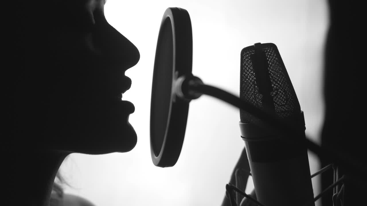 Professional singer in front of a microphone performing a song in studio. Attractive profile view of a female face singing. Close-up. Black and white video