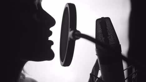 professional singer in front of a microphone performing a song in studio. attractive profile view of a female face singing. close-up. black and white video