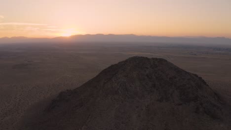 aerial orbit around mojave desert mountain butte during pink sunrise