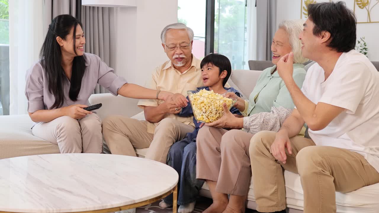 A joyful family of five enjoys popcorn together in a bright, modern living room. Warm lighting enhances the cheerful atmosphere