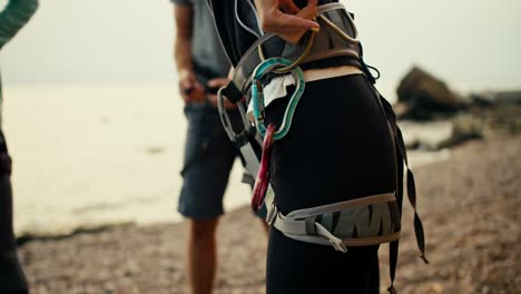 Shooting-close-up-of-a-girl,-A-rock-climber-puts-a-special-harness-on-her-belt-that-will-hold-her-while-climbing-a-rock-on-a-rocky-beach-by-the-sea.-Rock-Girl-prepares-to-climb-the-mountain-and-puts-on-the-appropriate-equipment