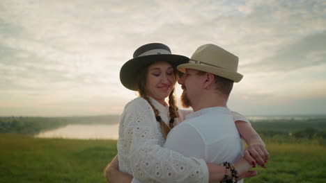 a loving couple embraces tenderly in a grassy field at sunset, both wearing matching white outfits and hats. they gaze into each other's eyes with affection of the golden light