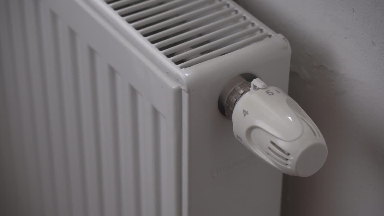 Reducing radiator or heating thermostat temperature, hand closeup, saving money during economic crisis
