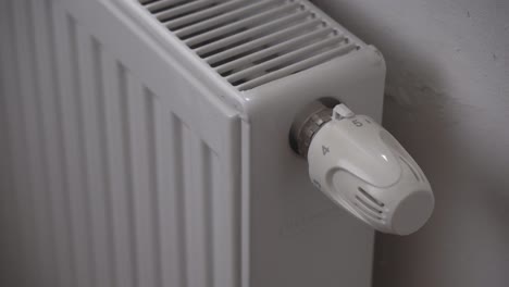 reducing radiator or heating thermostat temperature, hand closeup, saving money during economic crisis