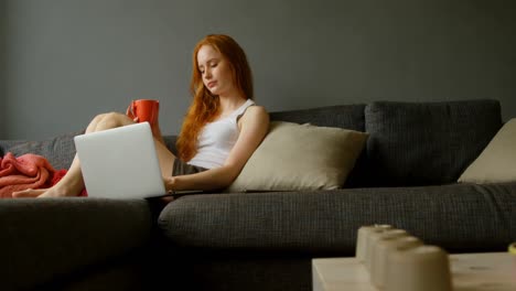 mujer tomando café mientras usa portátil en la sala de estar 4k