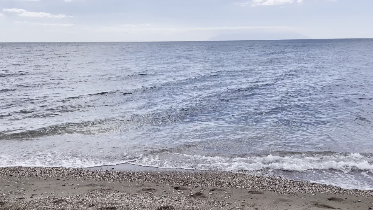 Relaxing seaside view of small waves rolling onto a sandy beach with seashells and footprints, perfect for coastal, travel, and nature themes