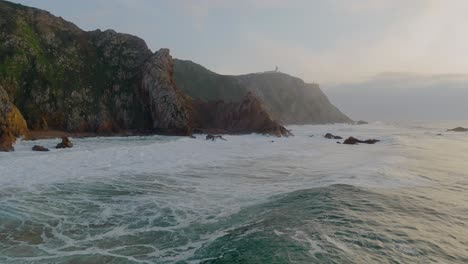 Rock-cliffs-on-Atlantic-Ocean-and-lighthouse-at-sunset,-Portugal