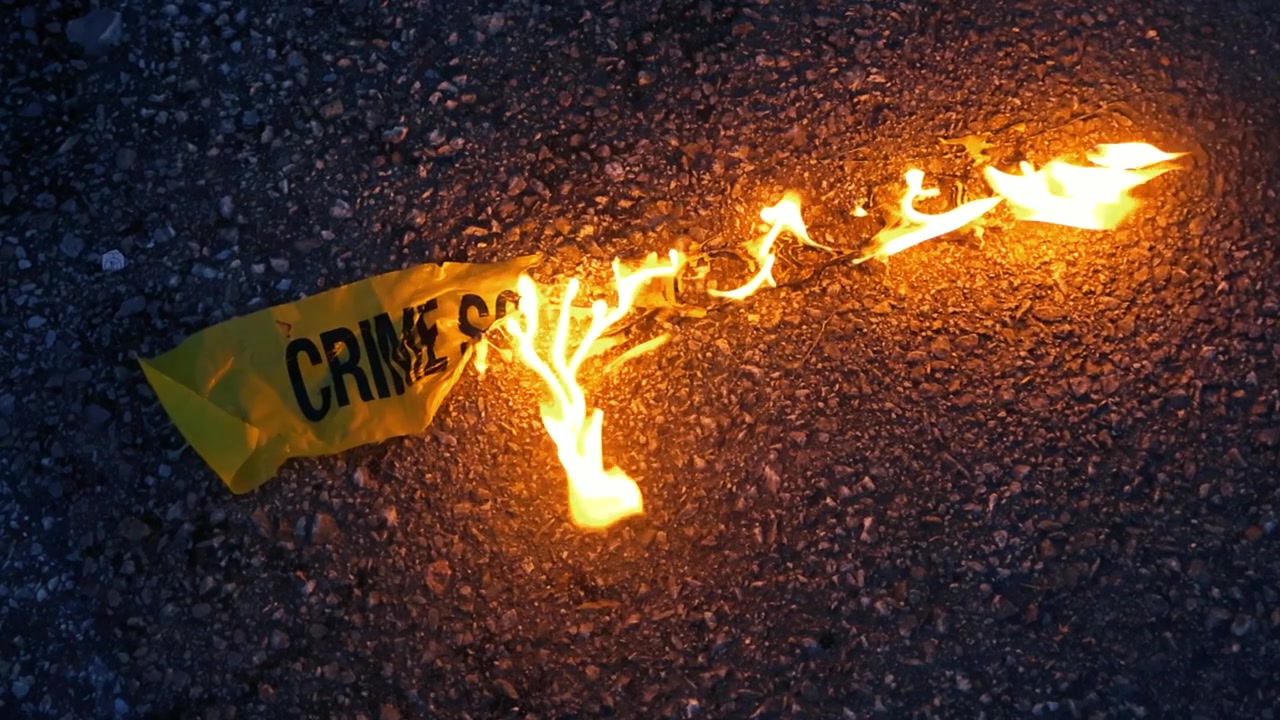 Yellow police tape with crime scene written on it burning with bright flames on the dark asphalt, symbolizing the destruction of evidence or the end of an investigation