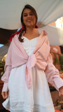 teenage girl in pink plaid shirt and white dress at a fruit stand