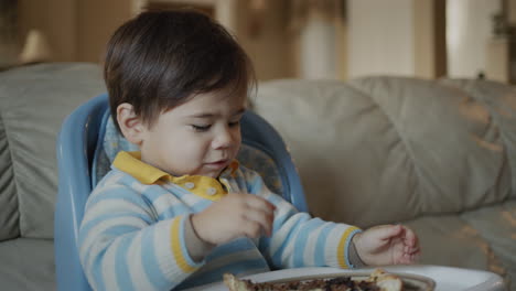 asian baby eats pizza, sits on the baby's feeding table