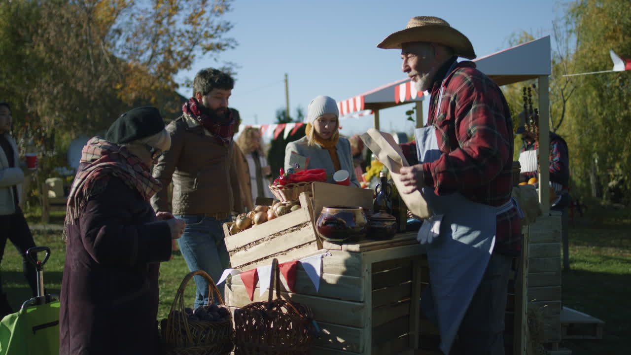 Senior Farmer Selling Products at Autumn Fair Senior Farmer Selling Fruits and Vegetables at the Stall Elderly Woman Puts Products in Paper Eco Bag Local Farmers Market or Autumn Fair Outdoors Agriculture Point of Sale system