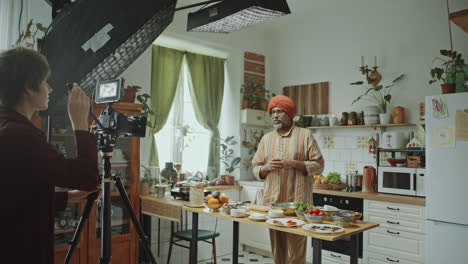 female camera operator filming indian food blogger explaining recipe in kitchen