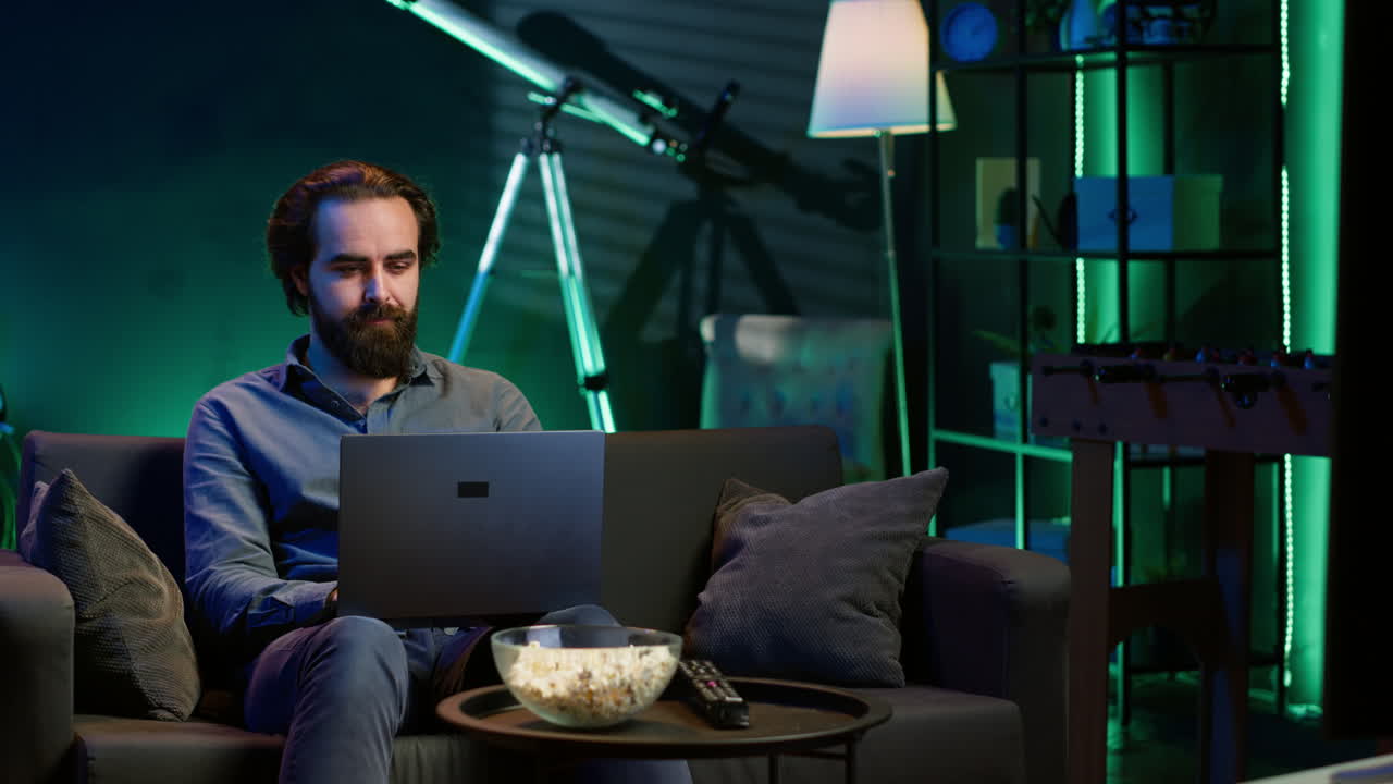 Freelancer working on laptop while watching TV in apartment office