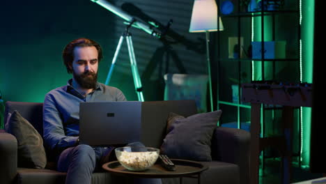 freelancer trabajando en una computadora portátil mientras ve la televisión en la oficina del apartamento