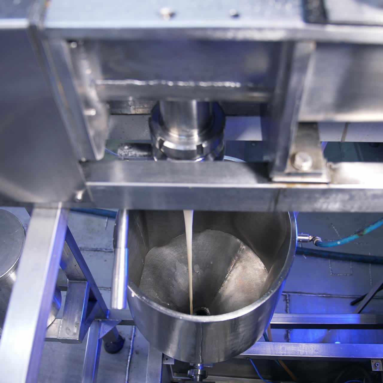 Thick creamy condensed milk being poured from a pipe into a metal tank. Confectionery production line at food factory