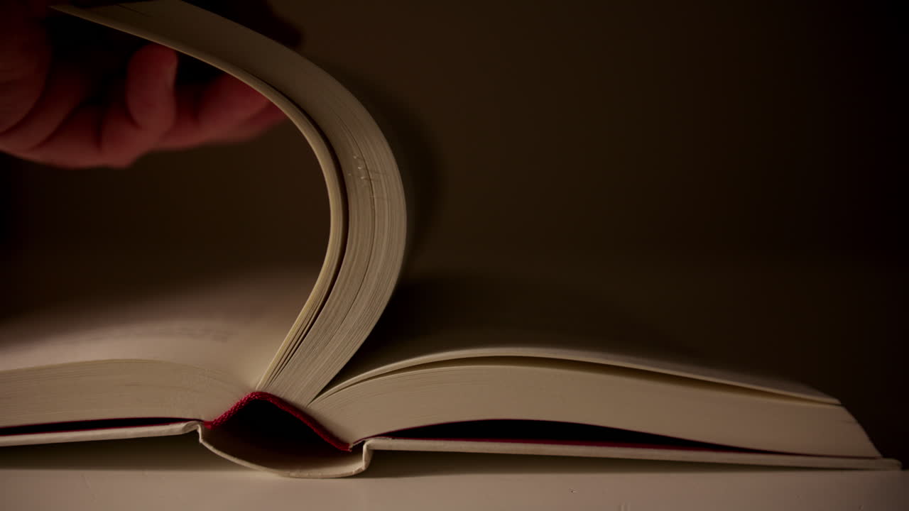 Primo piano di un libro aperto mentre una pagina viene girata lentamente, formando una forma curva in una luce soffusa. Atmosfera di lettura e narrazione tranquilla e senza tempo