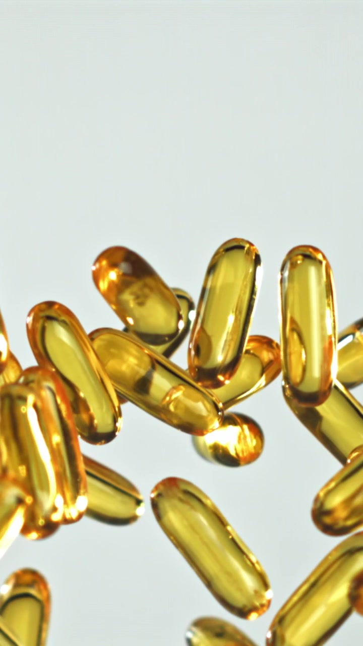 Primo piano di capsule dorate di Omega-3 che galleggiano su sfondo bianco