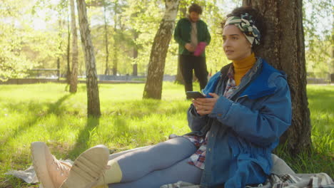 woman using smartphone and petting corgi in park