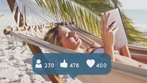 Animation-of-speech-bubble-with-people,-like-and-love-icons-and-numbers-over-woman-reading-on-beach