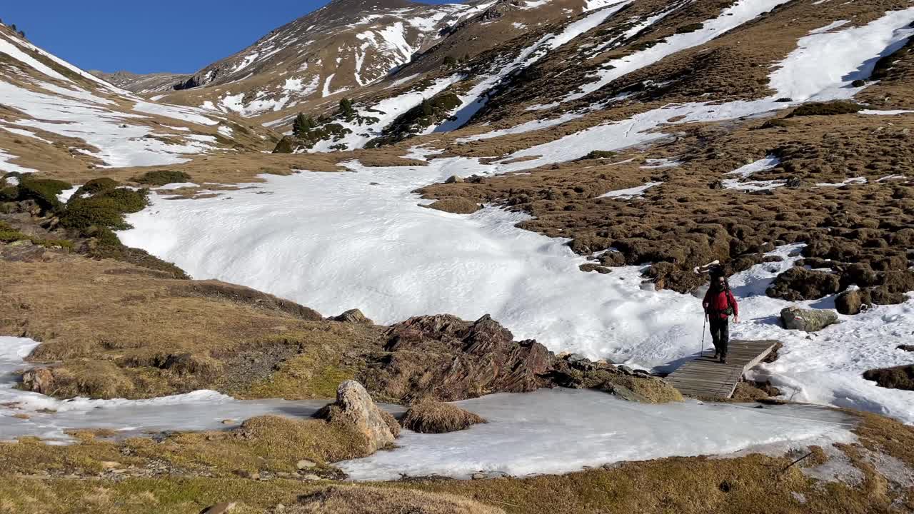 Stunning 4K shot of a solo hiker crossing a frozen wooden bridge in the Pyrenees, fully geared for a remote winter expedition. A breathtaking moment of alpine solitude and survival