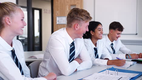 Line-Of-High-School-Students-Wearing-Uniform-Sitting-At-Desk-In-Classroom-Laughing