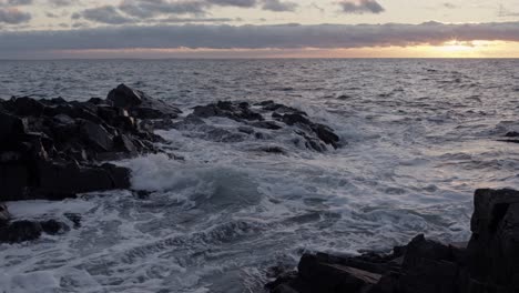 Stormy-ocean-waves-rolling-into-rocky-coast-line-at-sunset-in-slow-motion-and-4K