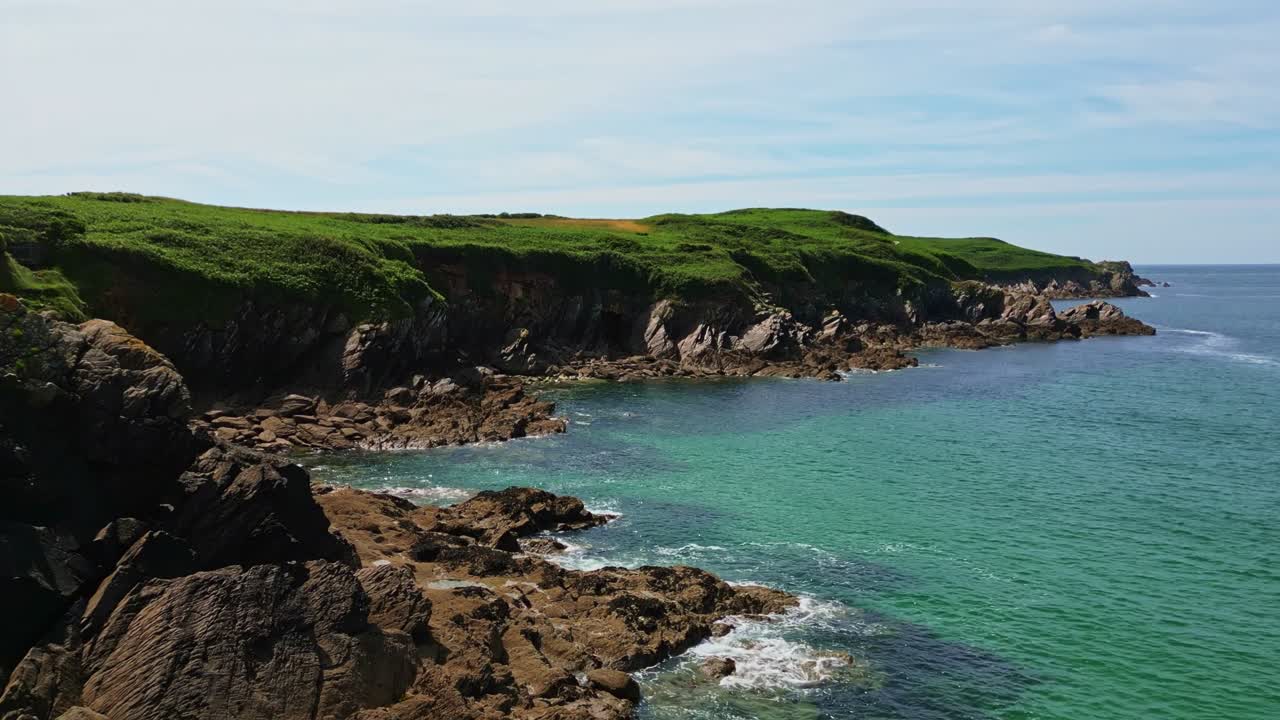 Low drone forward shot over the Kermorvan Peninsula in Le Conquet, showing cliffs, waves, rocks, and green vegetation - Brittany France