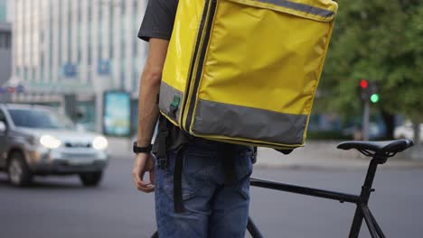 la entrega de pie con la bicicleta, esperando el tráfico ligero de la ciudad