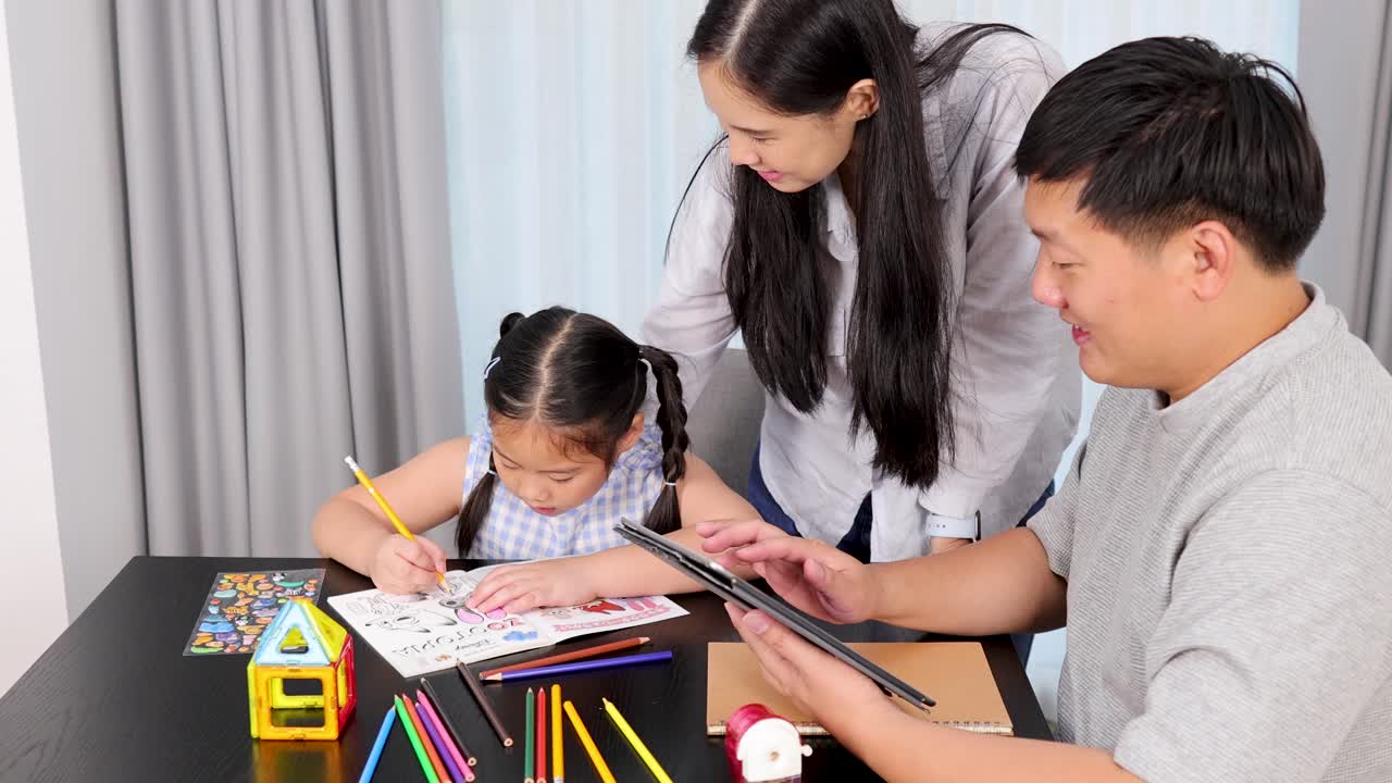 A family enjoys creative time together, with a child drawing and parents engaging with technology in a bright room