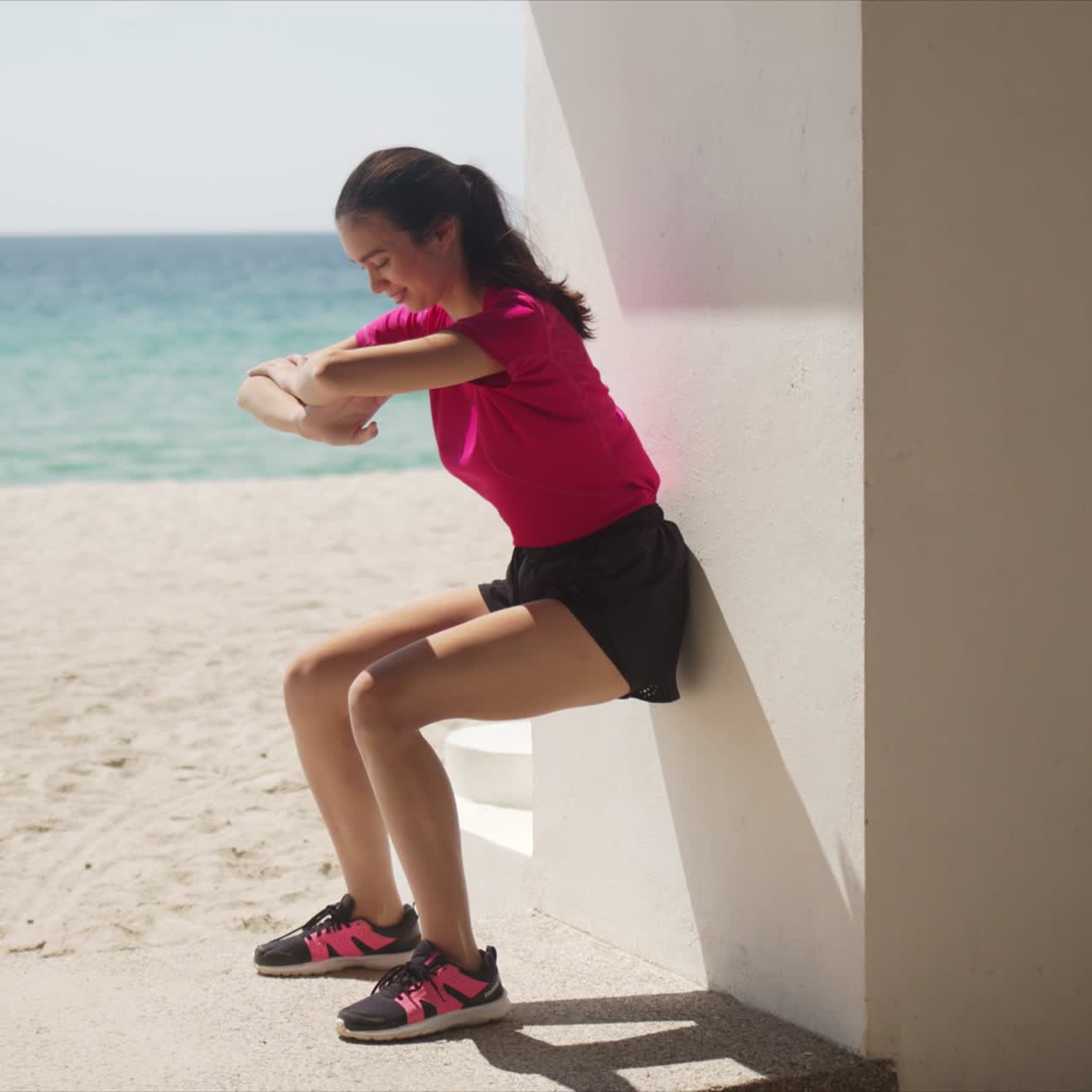 Giovane donna che esegue squat contro il muro sulla spiaggia