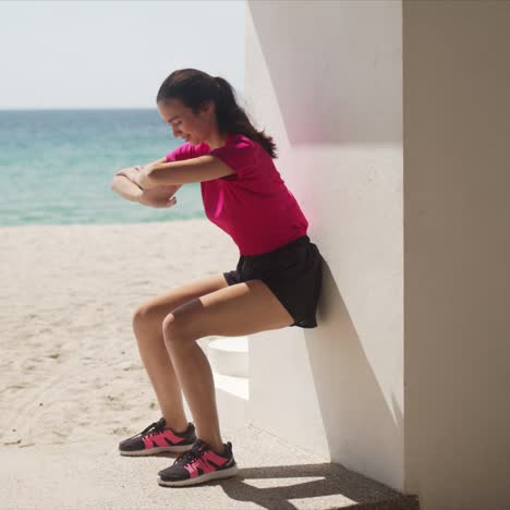 young woman doing wall squats on beach