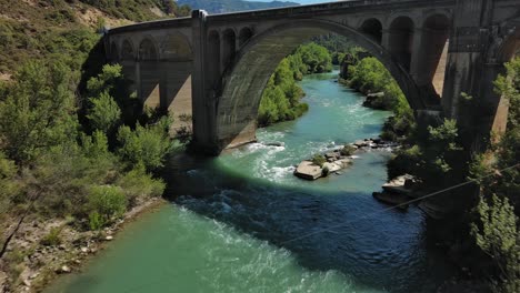 murillo de gallego bridge in huesca over a turquoise river surrounded by greenery, aerial view