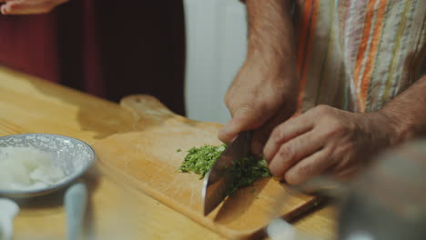 hands of chef chopping fresh herbs on cutting board in kitchen