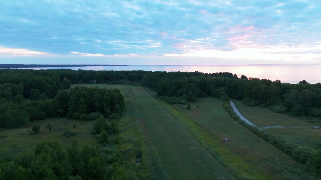 Taking flight from a rural airfield and revealing a calm sea and coastline.