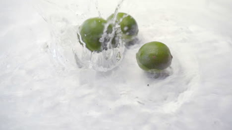 slomo of limes falling into water on white backdrop