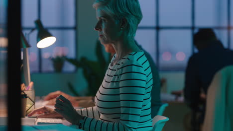 mature business woman working late typing using desktop computer diverse team corporate project in start up office workspace