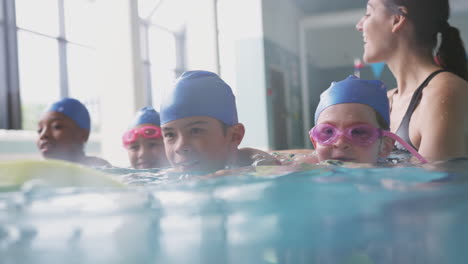female coach in water with children gives swimming lesson in indoor pool