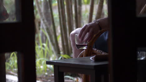 Man-Relaxing-Outside-Picks-Up-Glass-With-Alcoholic-Drink-In-It